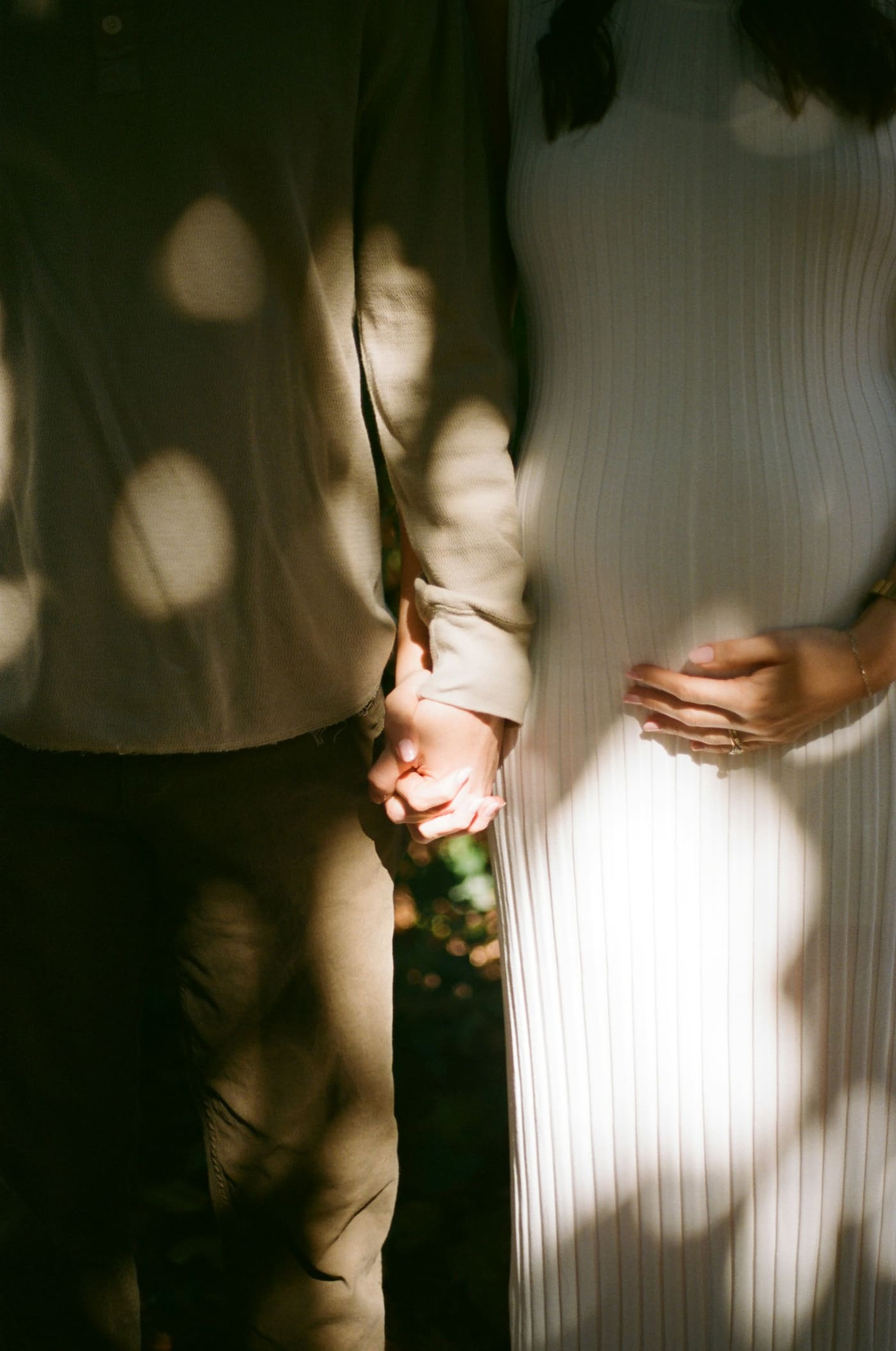 Expecting parents holding hands in sunlight